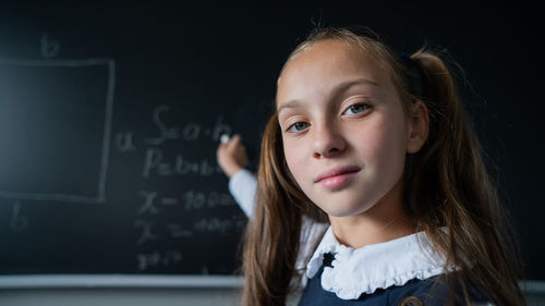 Portrait of a caucasian girl in the classroom. the schoolgirl writes the formula with chalk on the