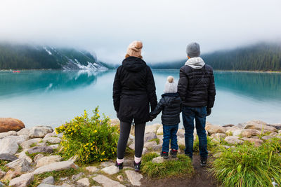 Rear view of friends standing by lake against sky