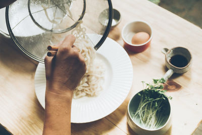 Cropped hand of woman pouring noodles in plate on table