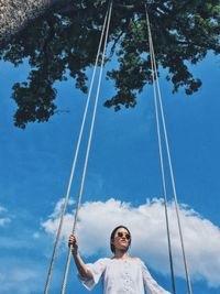 Low angle view of woman holding ropes while standing against sky