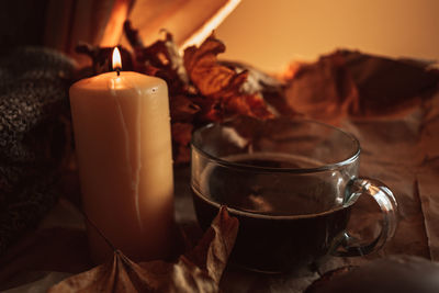 Burning yellow candle and large mug of black coffee in a cozy home autumn evening still life