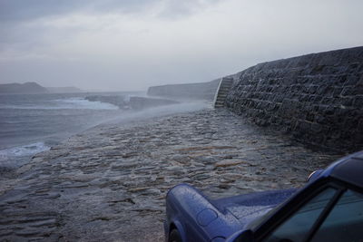 Scenic view of parked car in front of stormy beach