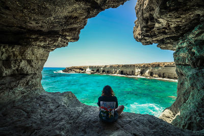 Rear view of woman sitting on rock in sea