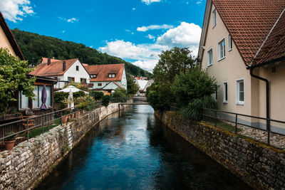 Houses by river amidst buildings against sky