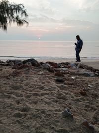 Man standing on beach against sky during sunset