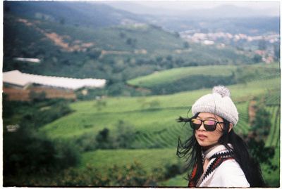 Young woman wearing sunglasses standing against landscape