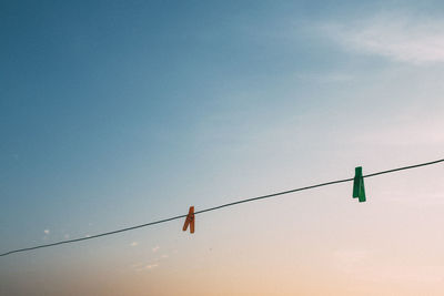 Low angle view of clothespin hanging on rope against sky during sunset