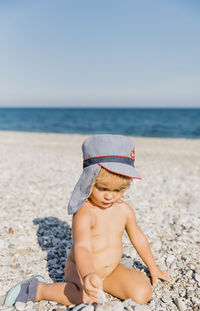 Shirtless girl playing at beach against clear sky