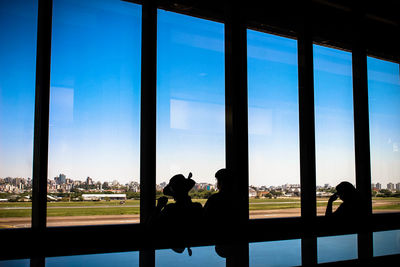 Silhouette people standing by window in waiting room at airport