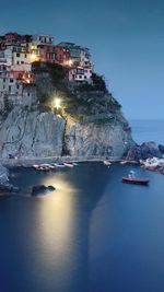 Illuminated buildings by sea against clear blue sky