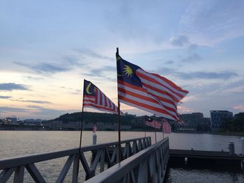 Flag by river against sky during sunset