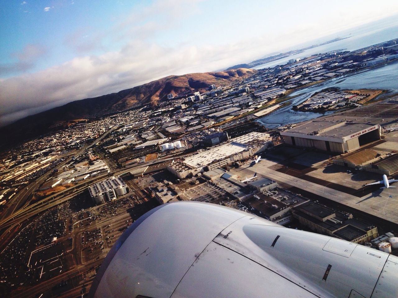 aerial view, airplane, building exterior, air vehicle, cityscape, sky, architecture, aircraft wing, built structure, city, high angle view, cloud - sky, landscape, mode of transport, transportation, crowded, part of, mountain, flying, travel