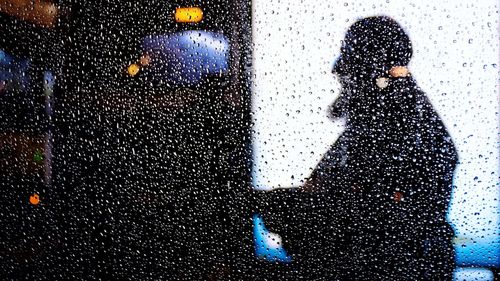 Silhouette man standing on wet window in rainy season