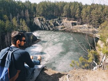 Man sitting on rock by river in forest