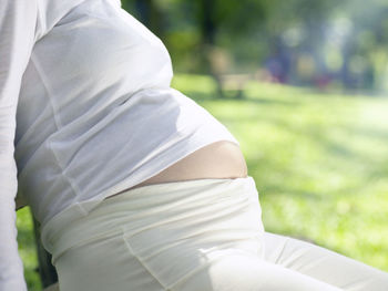 Midsection of pregnant woman sitting at park