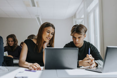 Multiracial male and female students sharing laptop at desk in classroom