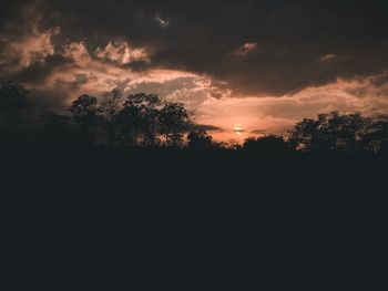 Silhouette trees on landscape against sky at sunset