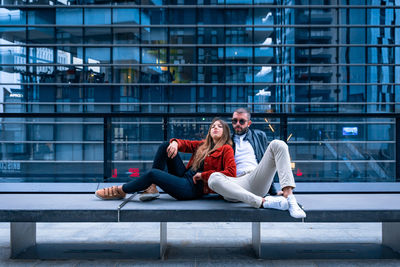 Young couple sitting on bench against building
