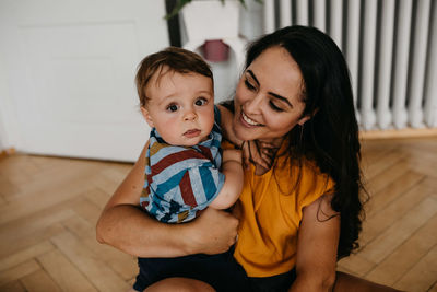 Smiling mother with baby boy sitting on wooden floor