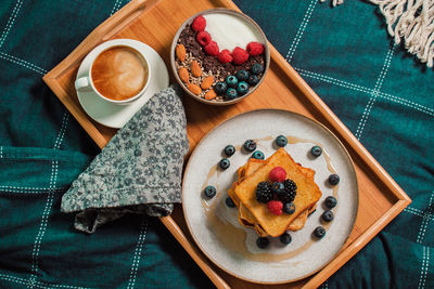 Breakfast in bed from above, yogurt bowl with berries, french toasts, coffee cup on wooden plate