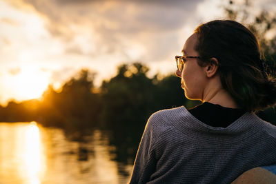 Portrait of young woman looking away against sky during sunset