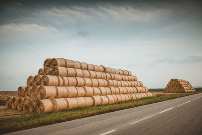 Hay bales on field by road against sky