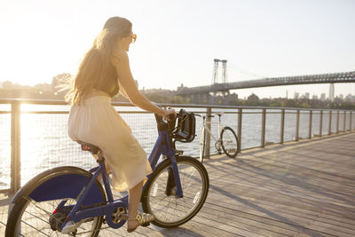 Happy woman riding bicycle on promenade during sunset