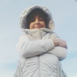 Low angle portrait of woman wearing winter jacket against sky