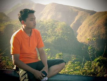 Young man looking away while sitting on mountain