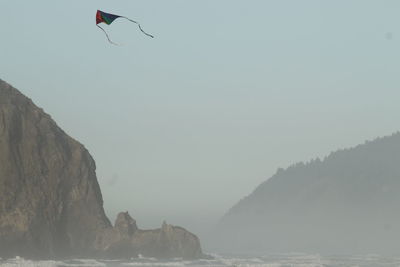 Person paragliding over sea against clear sky