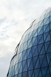 Low angle view of glass building against cloudy sky