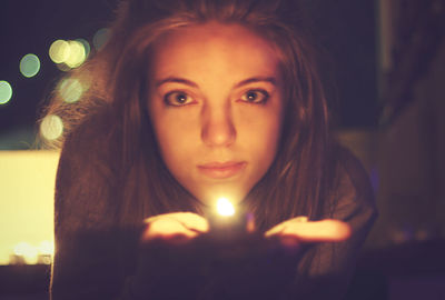 Portrait of beautiful woman holding lit tea light candle at night