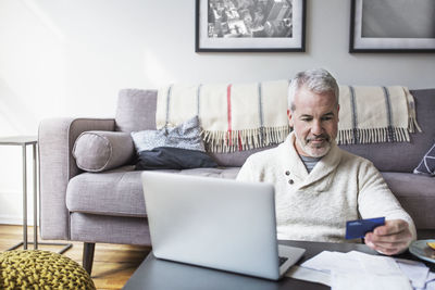 Mature man using credit card and laptop while shopping online at home