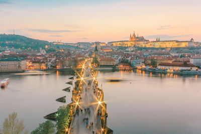 River by cityscape against sky during sunset