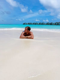 Full length of shirtless man relaxing on beach