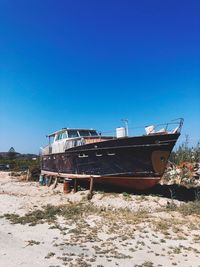 Abandoned ship moored on beach against clear blue sky