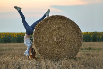 Woman doing handstand by hay bale during sunset