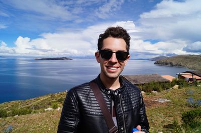 Portrait of smiling young man standing by sea against sky