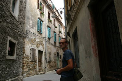 Portrait of man standing in alley amidst buildings