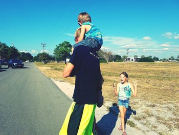 Father and kids enjoying summer on roadside against sky