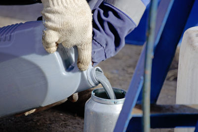 A gloved worker pours gray paint from a canister into a spray gun. preparation for painting works.