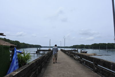 Rear view of man standing on pier over lake against sky