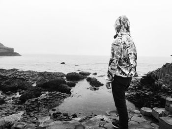 Man standing on rock by sea against sky