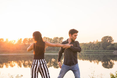 Friends standing by lake against clear sky