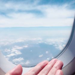 Cropped image of hand on airplane window against sky