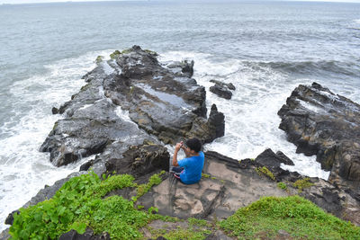 Boy sitting on rock by sea