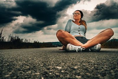 Surface level view of woman sitting on road against cloudy sky