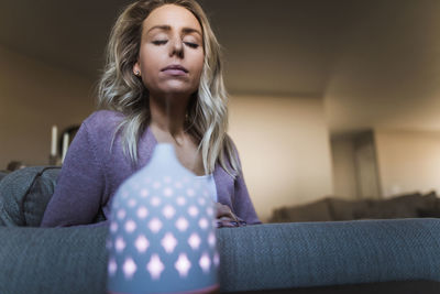 Young woman looking away while sitting on sofa at home