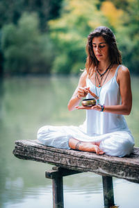 Woman holding singing bowl while doing yoga at lake