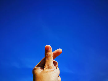 Close-up of cropped hand gesturing against blue sky